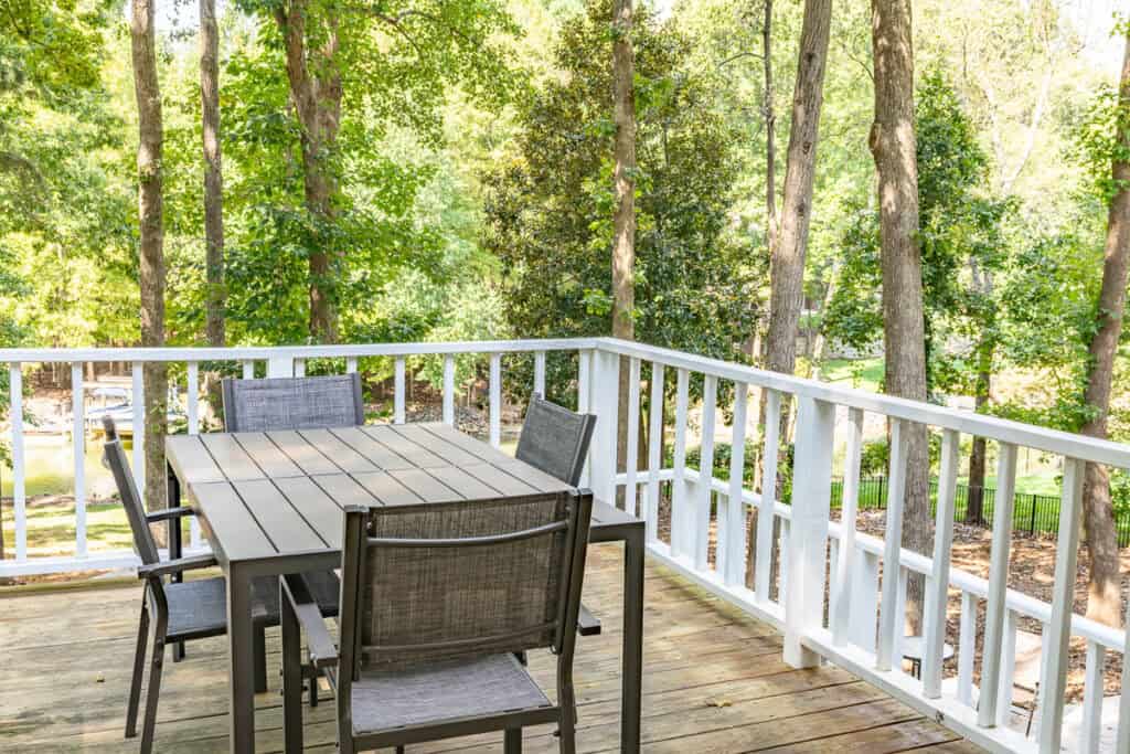 An outdoor dining area on a wooden deck, surrounded by trees and overlooking a serene backyard.