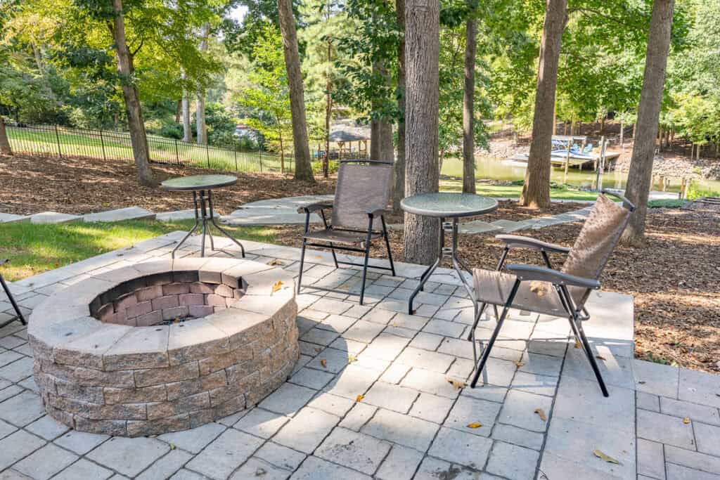 A charming fire pit surrounded by patio chairs and small tables, nestled in a landscaped backyard.