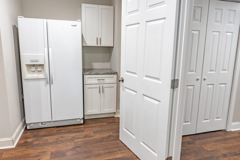 Pantry and utility area with a large white refrigerator, built-in cabinets, and wood flooring.