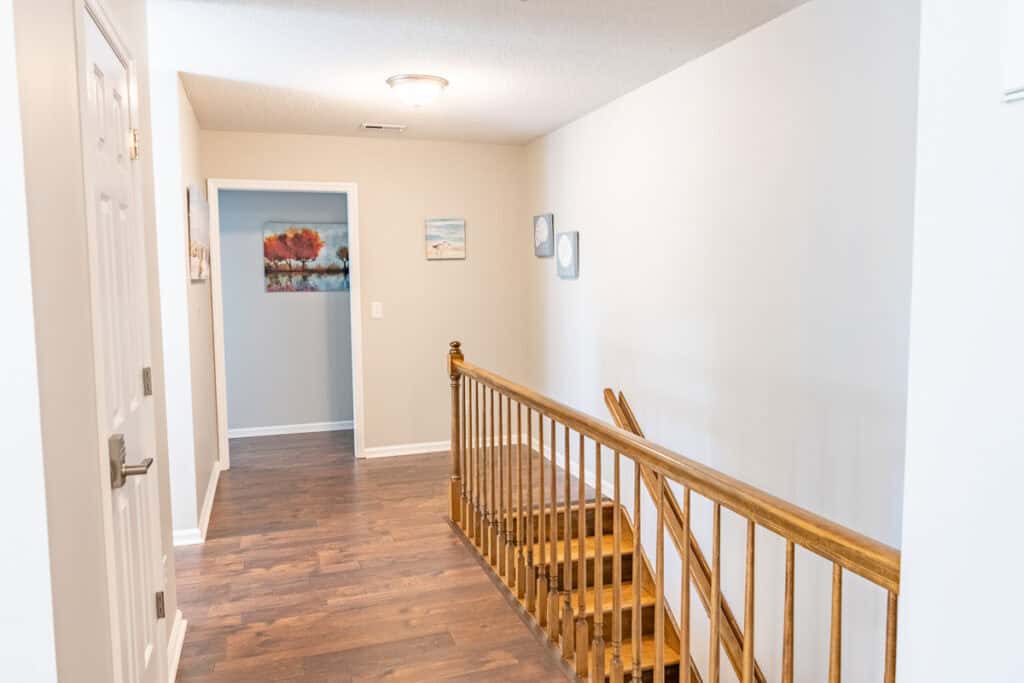 Upper floor hallway featuring wood floors, neutral walls, and artwork for added warmth.