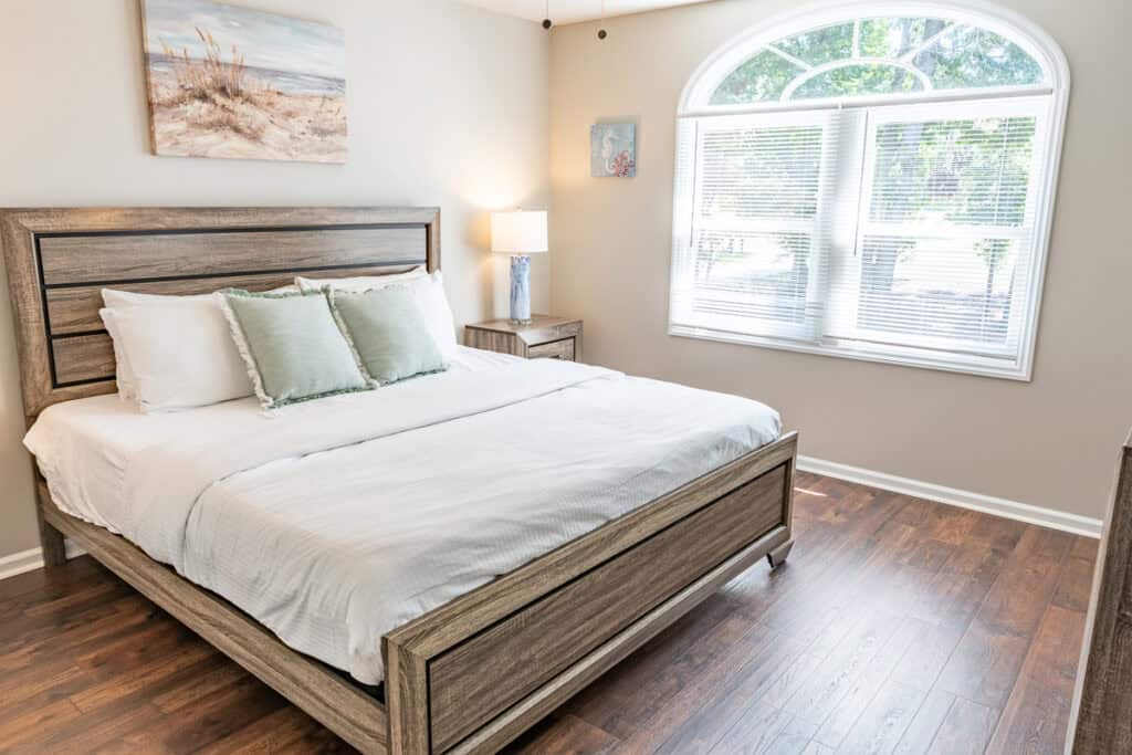 Spacious bedroom with a king-size bed, neutral decor, and a large arched window allowing natural light to brighten the room.
