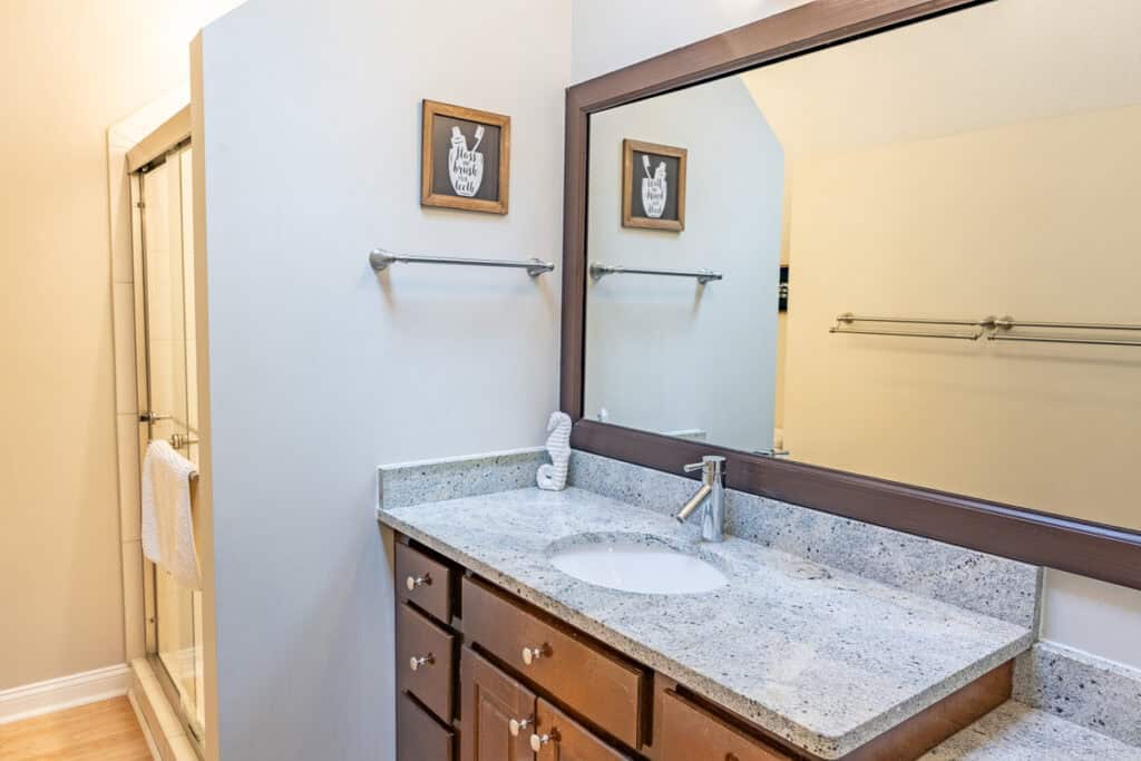 Elegant bathroom with a granite countertop, wide mirror, and a walk-in shower.