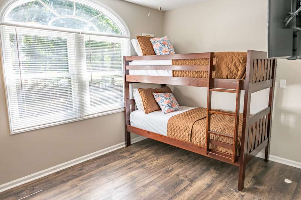 Bright and airy bedroom with wooden bunk beds, colorful bedding, and a large arched window.