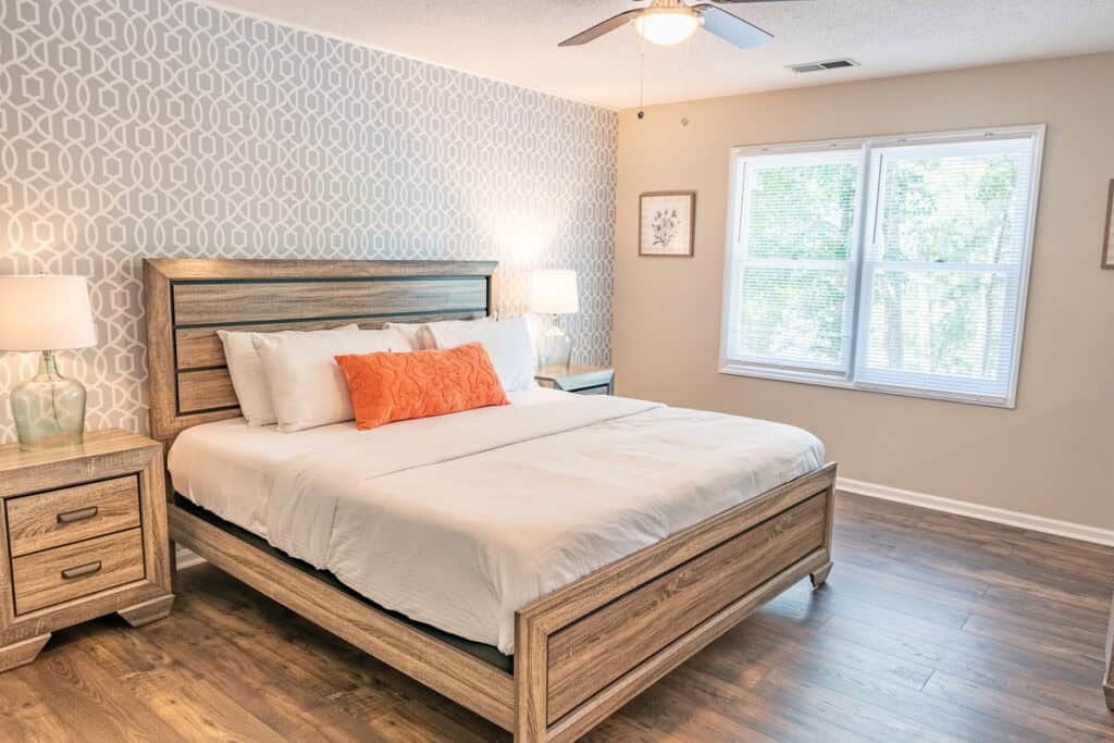 Bedroom with Orange Accent Pillow A bright and spacious bedroom featuring a king-sized bed with clean white bedding, complemented by an orange accent pillow and modern decor on the walls.