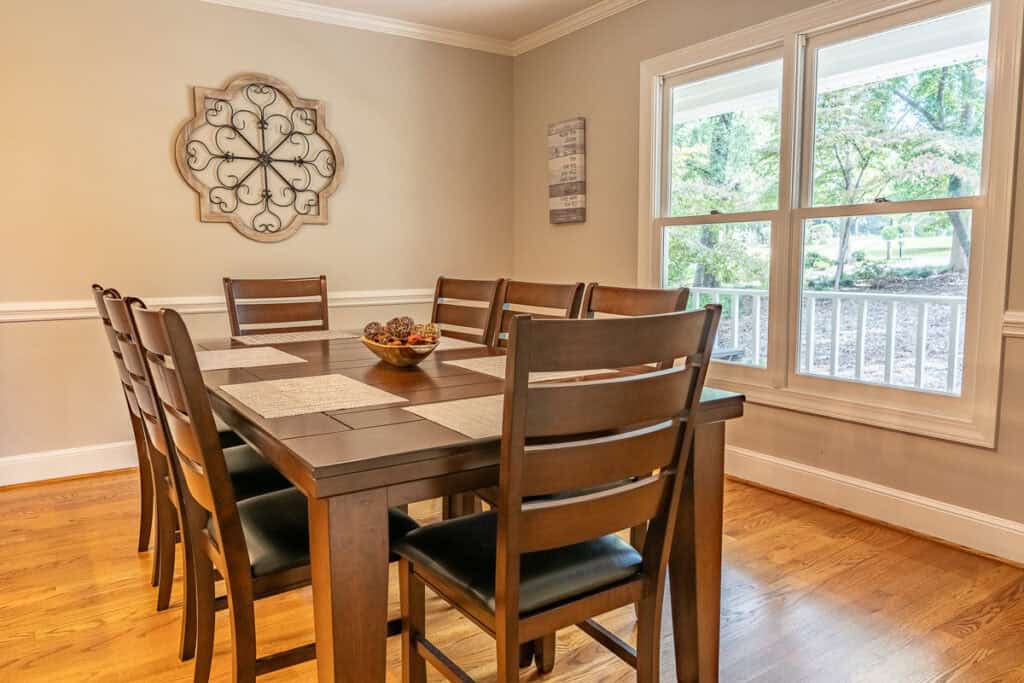 A formal dining room with a dark wooden table and chairs, situated near a large window offering scenic views of the outdoors.