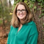 a woman in a green shirt and glasses smiling