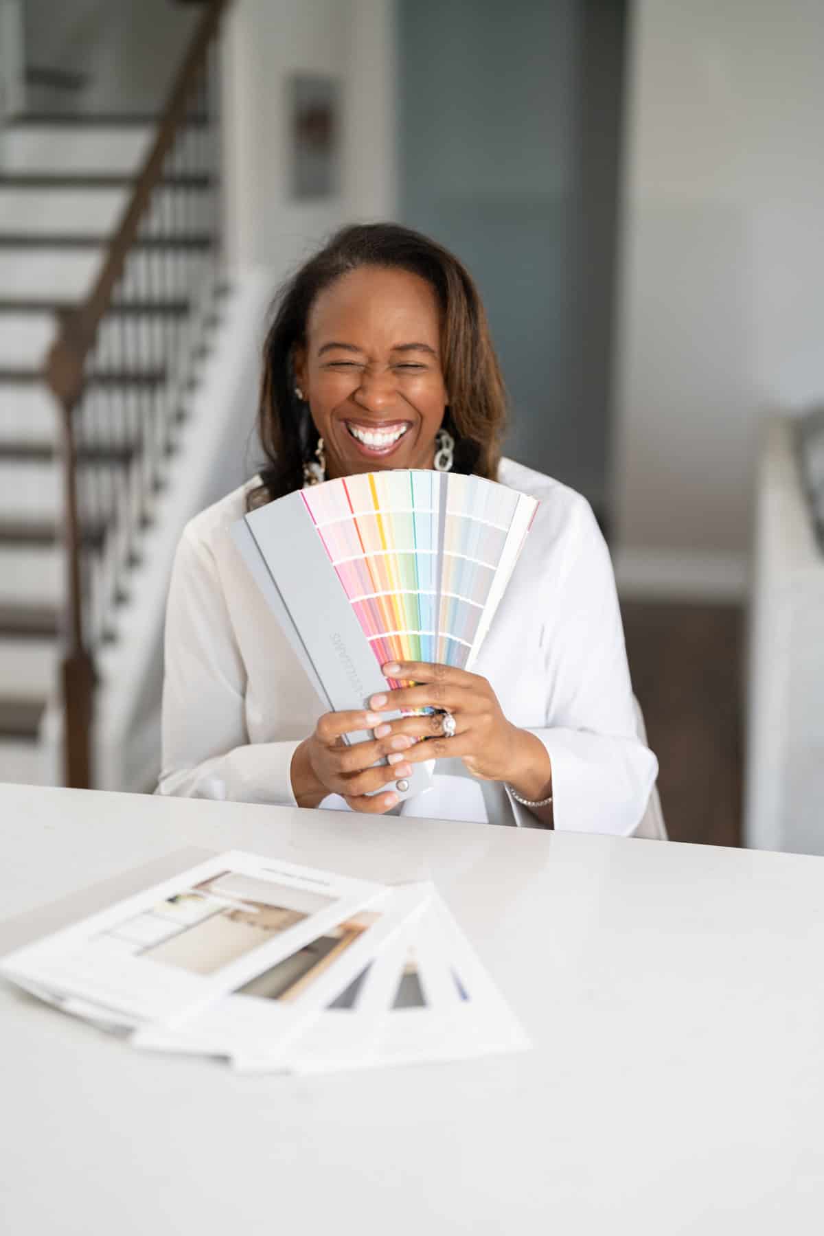 a woman laughing while holding a fan of color swatches